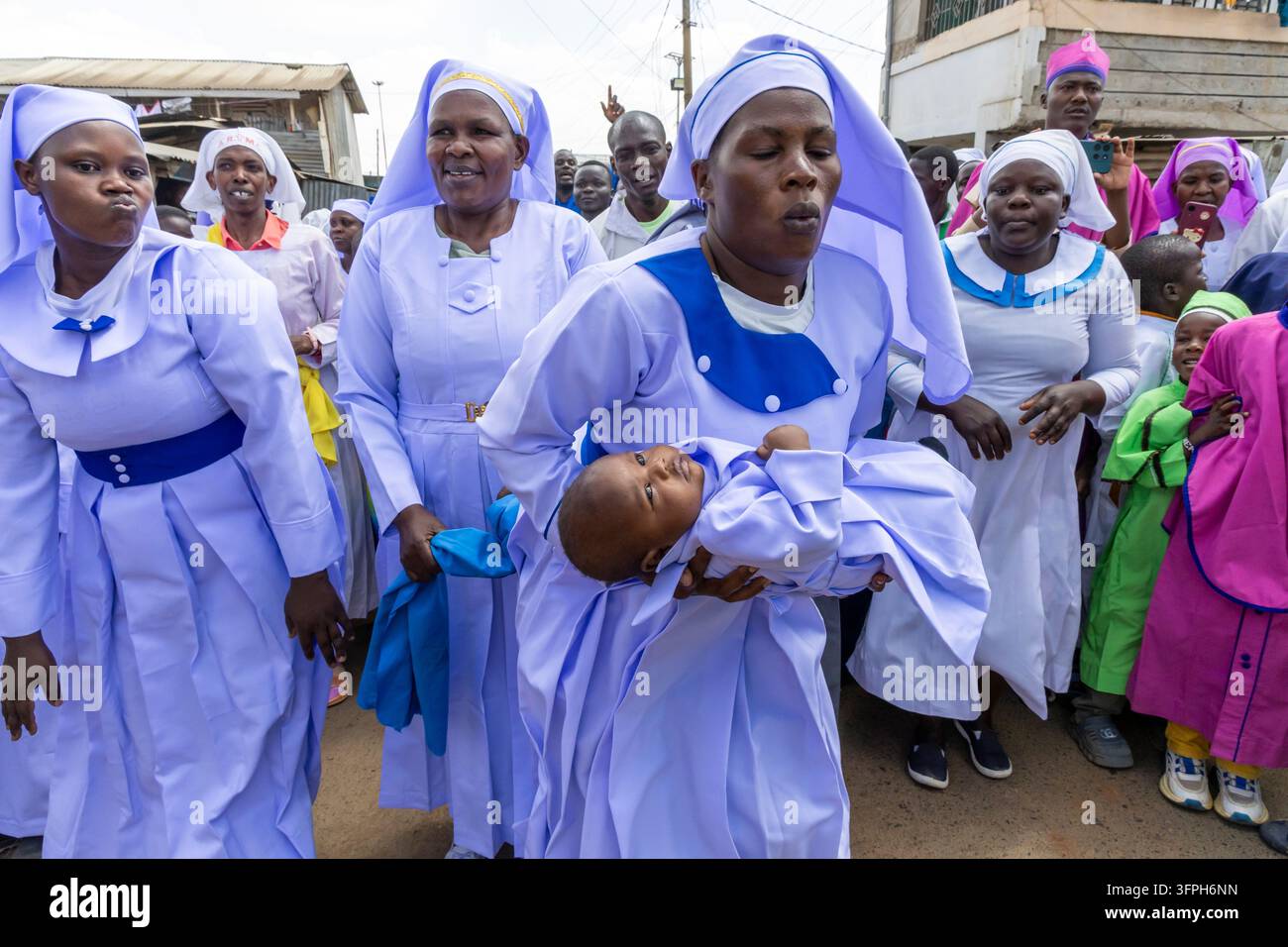 Donne in veli lilla che cantano e camminano mentre una porta un bambino in una processione battesimale a Kibera, Contea di Nairobi, Nairobi, Kenya Foto Stock