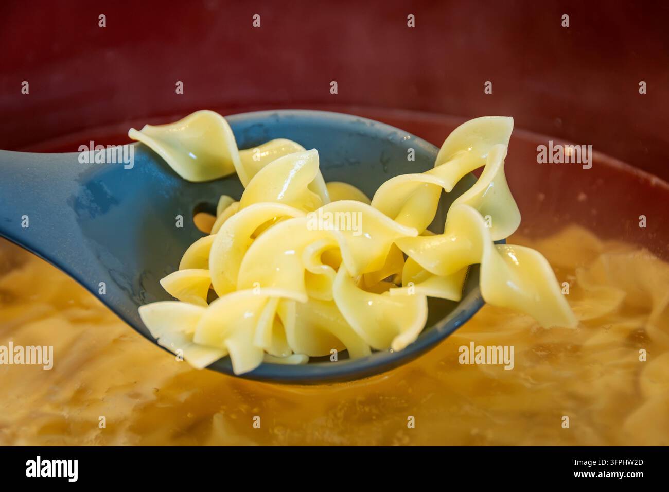 Meal Prep Pollo Alfredo facile: primo piano di spaghetti alle uova a spirale cotti sollevati su un cucchiaio scanalato sopra l'acqua calda. Foto Stock