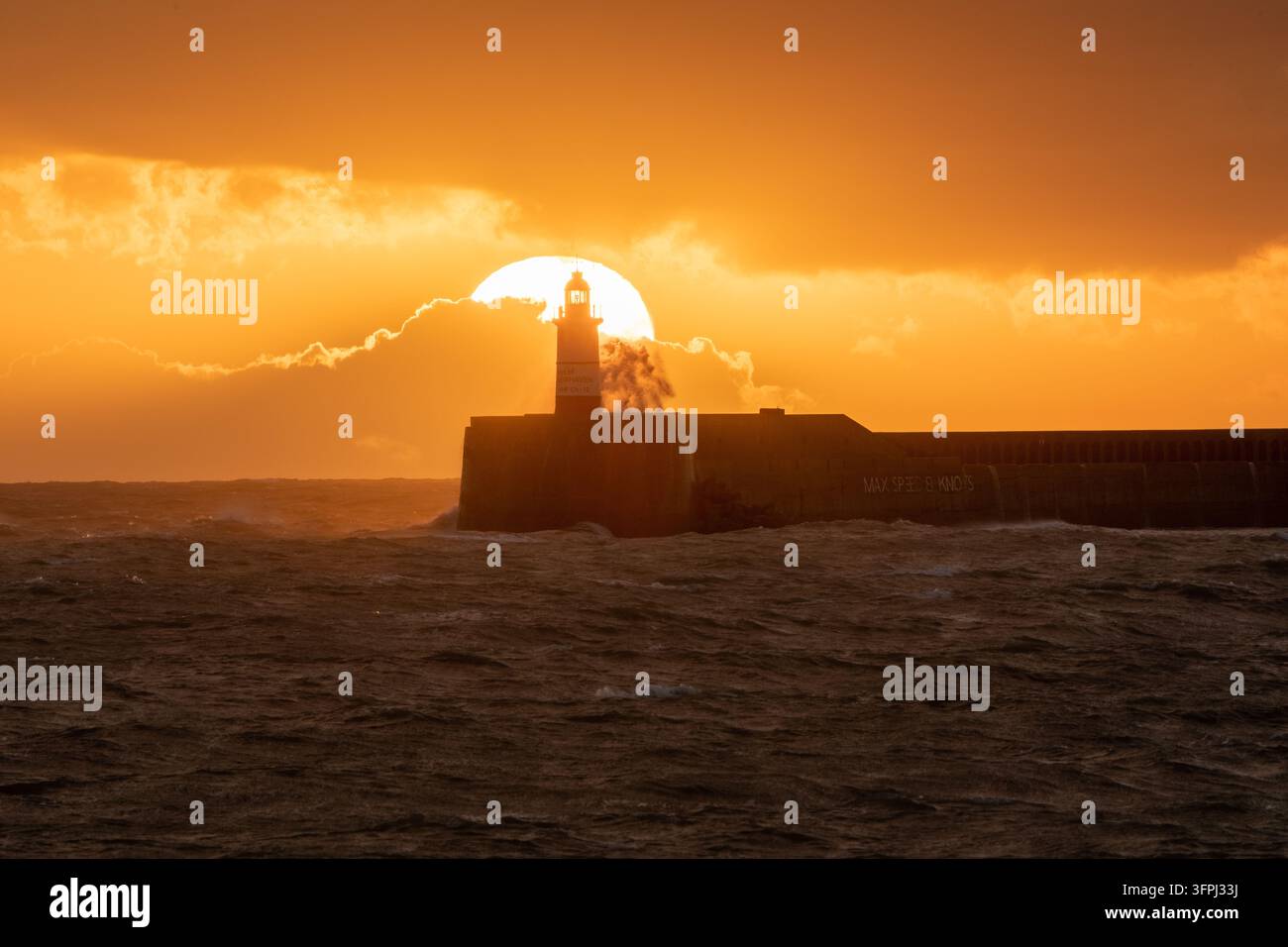 Silhouette drammatica al tramonto del faro storico di Newhaven Breakwater durante una tempesta marina agitata nell'East Sussex, Inghilterra. Foto Stock
