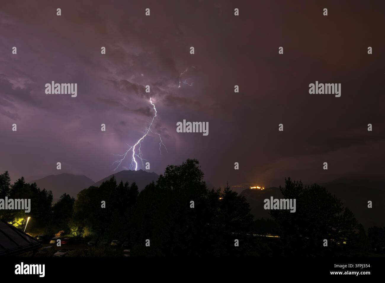 Drammatico fulmine che colpisce una vetta montuosa di notte durante una violenta tempesta estiva su una valle alpina boscosa. Foto Stock