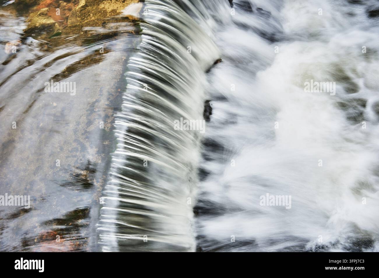 Acqua sfocata in movimento che cade su una diga, leggermente inclinata Foto Stock