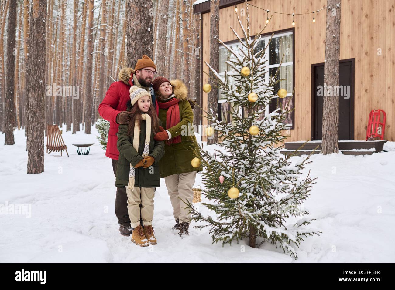 Famiglia con figlia che decora l'albero di Natale nella foresta invernale Foto Stock