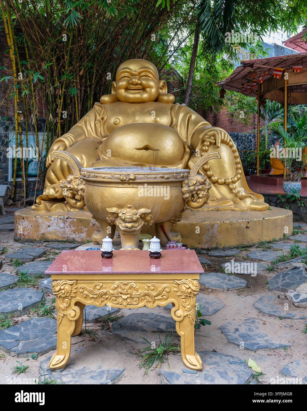 Statua dorata di Buddha sorridente con un bruciatore di incenso e un tavolo ornato nel cortile della pagoda Phap Lam a Da Nang, Vietnam Foto Stock
