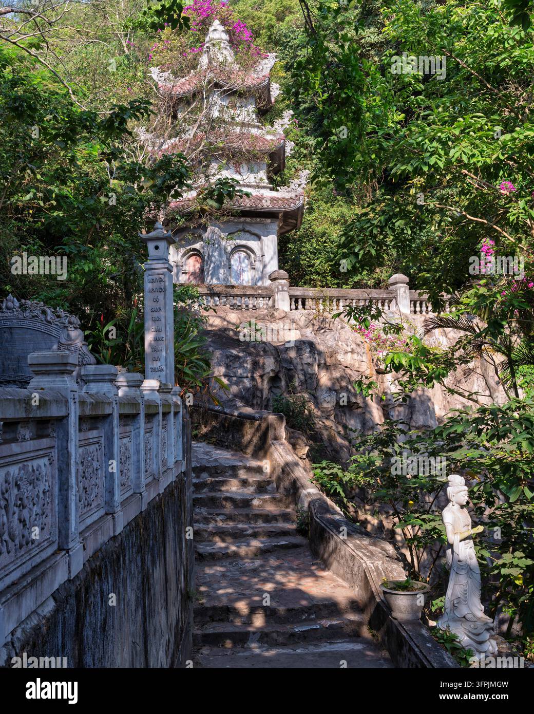 Pagoda tradizionale in pietra e scala in pietra circondati da alberi verdi rigogliosi e da una statua di divinità bianca sulle Montagne di Marmo a Da Nang, Vietnam Foto Stock