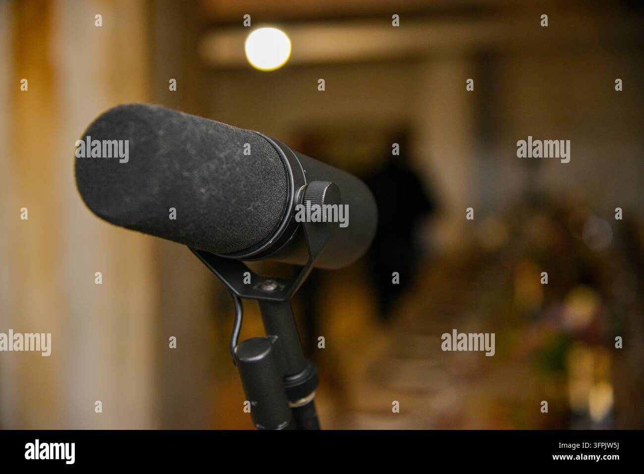 Prima piani di un microfono da studio professionale nero con parabrezza in schiuma, fotografato al chiuso con illuminazione cinematografica calda e profondità di campo poco profonda Foto Stock