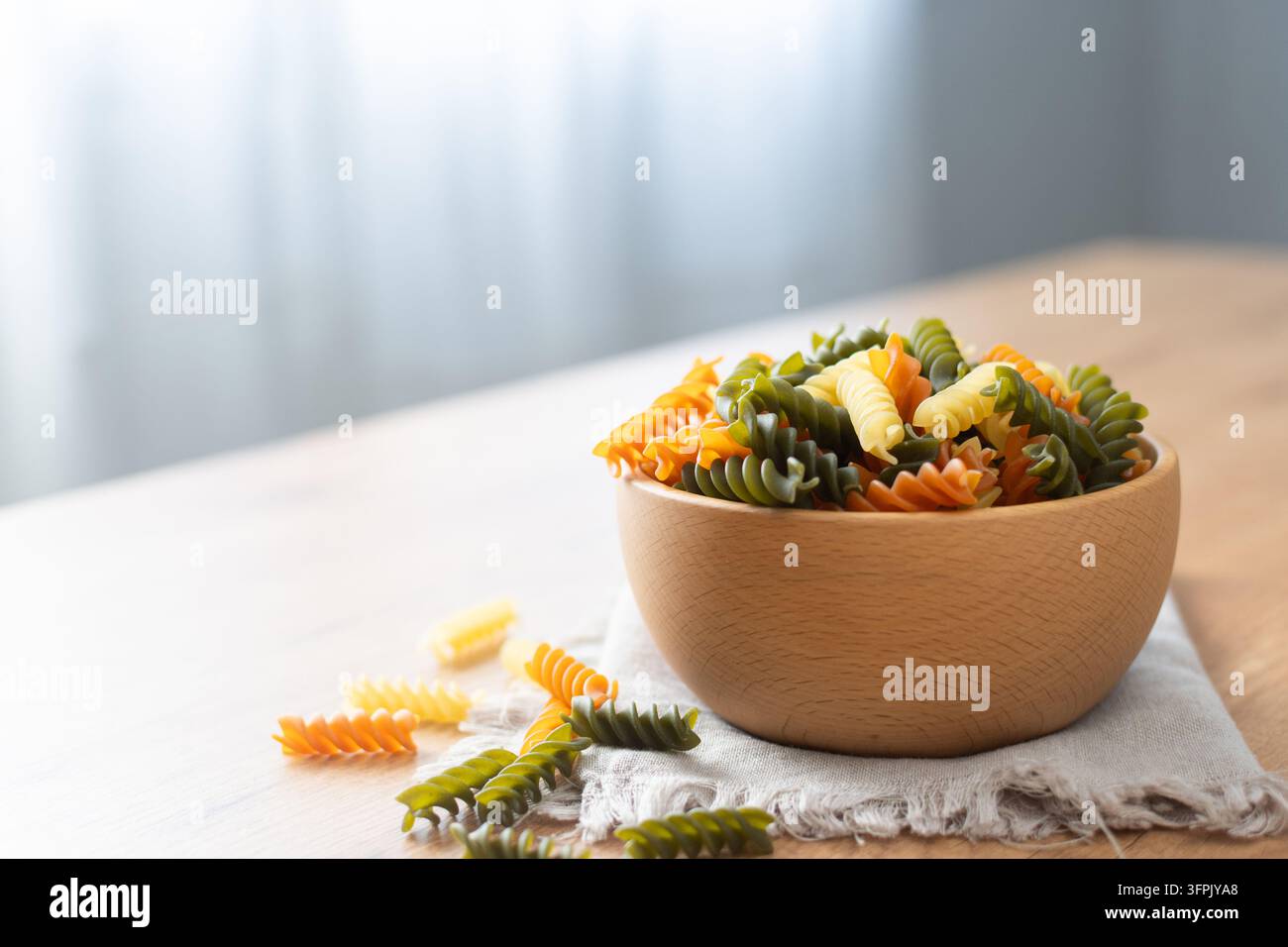 Pasta fusilli tricolore asciutta in una ciotola su tavolo di legno Foto Stock