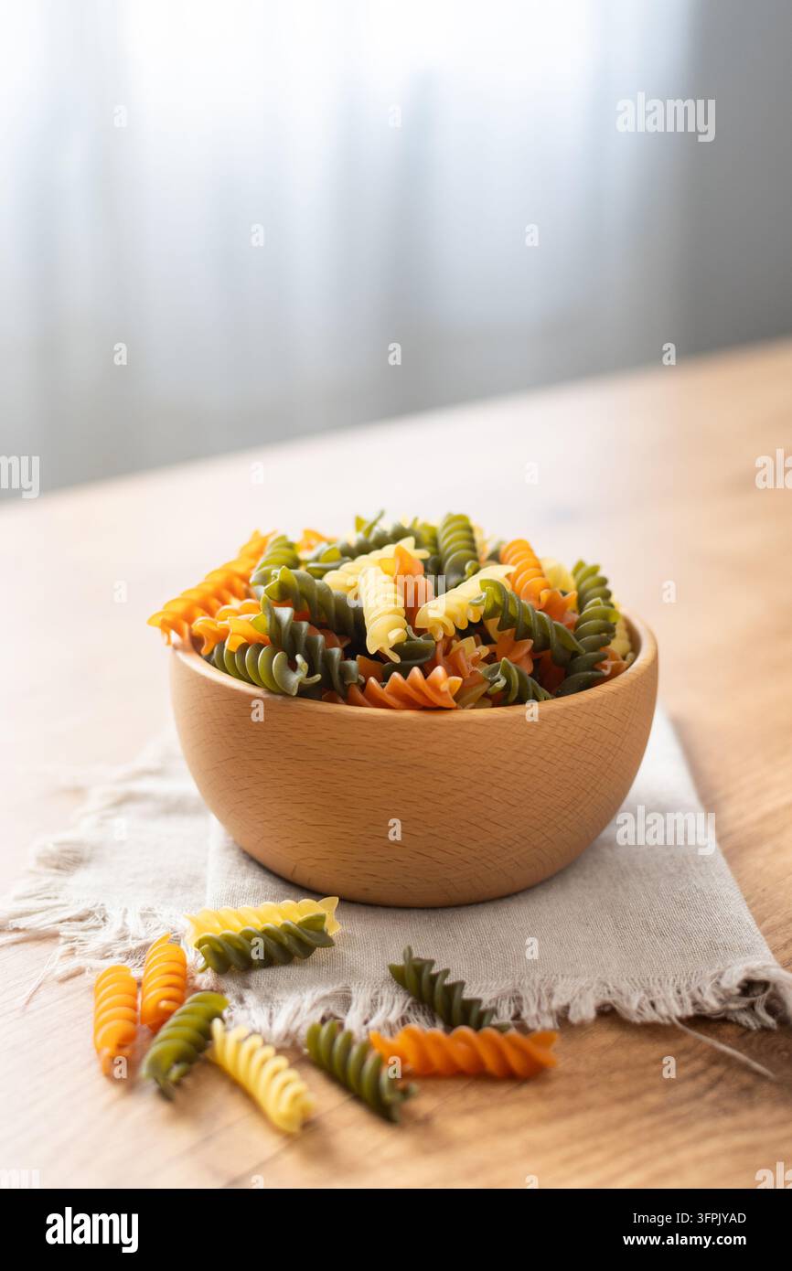 Pasta fusilli tricolore asciutta in una ciotola su tavolo di legno Foto Stock