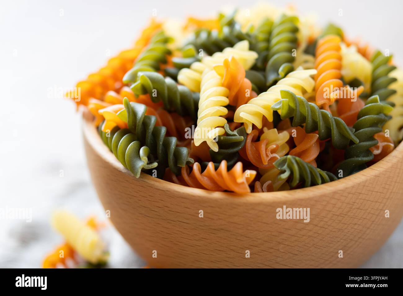 Pasta fusilli tricolore asciutta in una ciotola su tavolo di legno Foto Stock