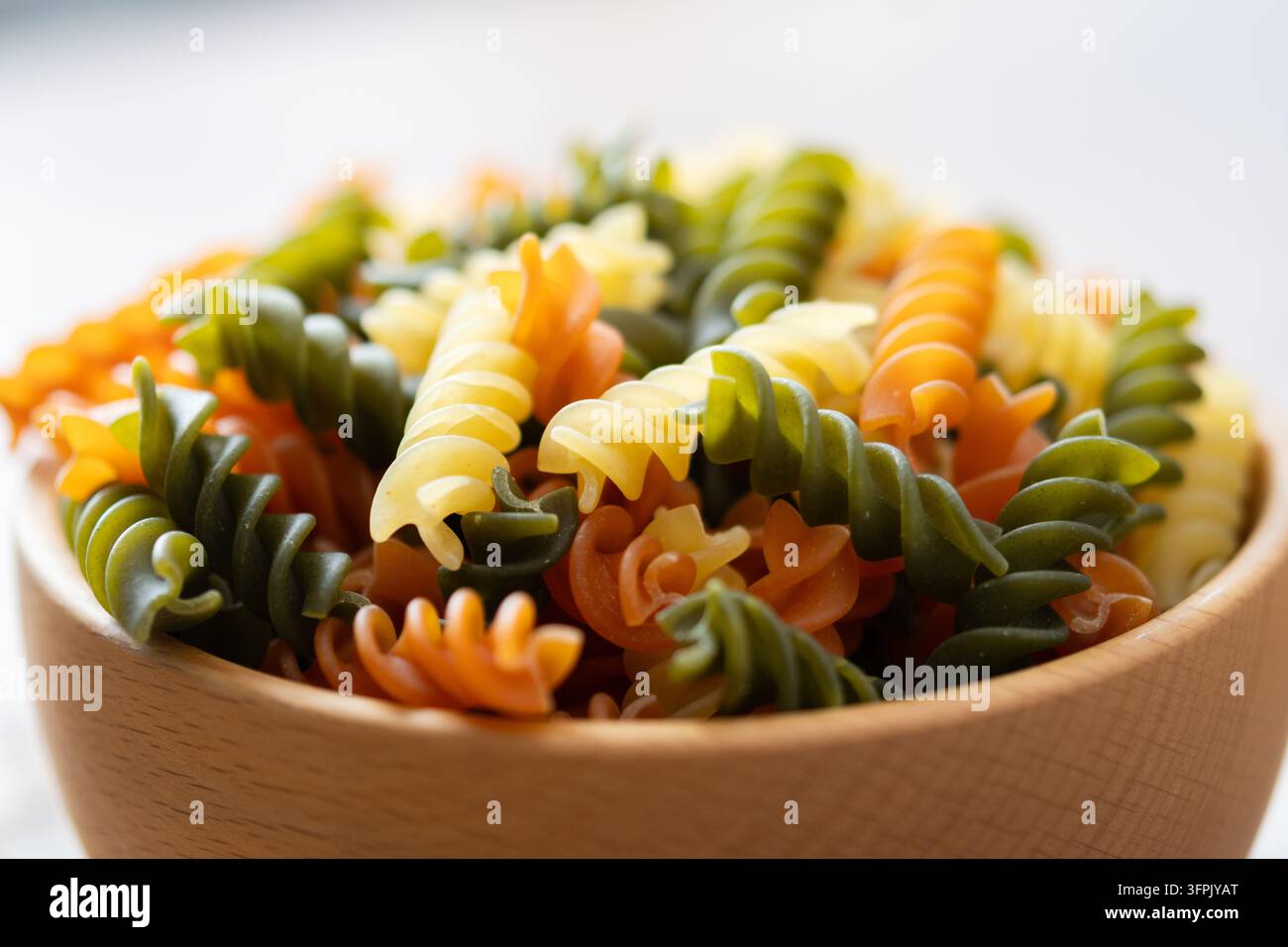 Pasta fusilli tricolore asciutta in una ciotola su tavolo di legno Foto Stock