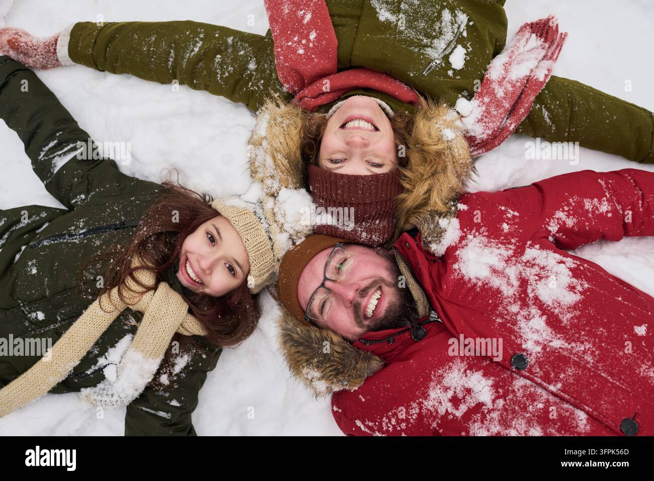 Ritratto di una famiglia felice sdraiata sulla neve durante le vacanze invernali Foto Stock