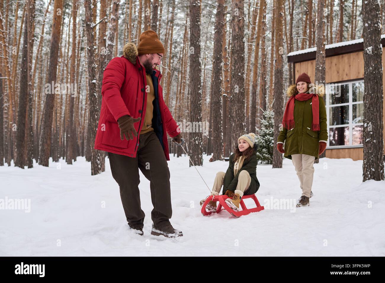 Padre che tira la figlia su uno slittino nella foresta innevata durante le vacanze invernali Foto Stock