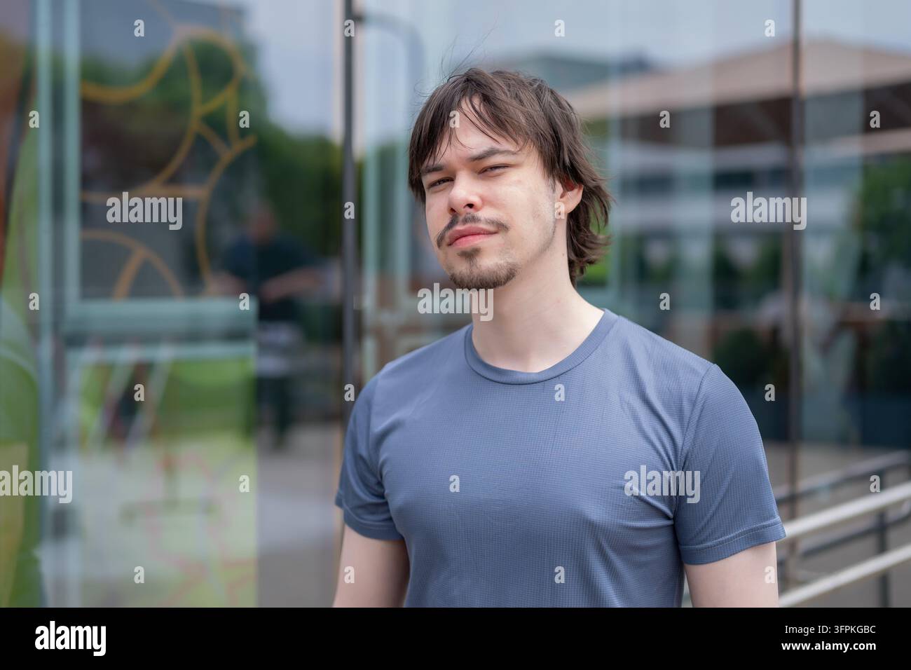 Un giovane uomo con una camicia blu si trova davanti a un moderno edificio in vetro. Foto Stock