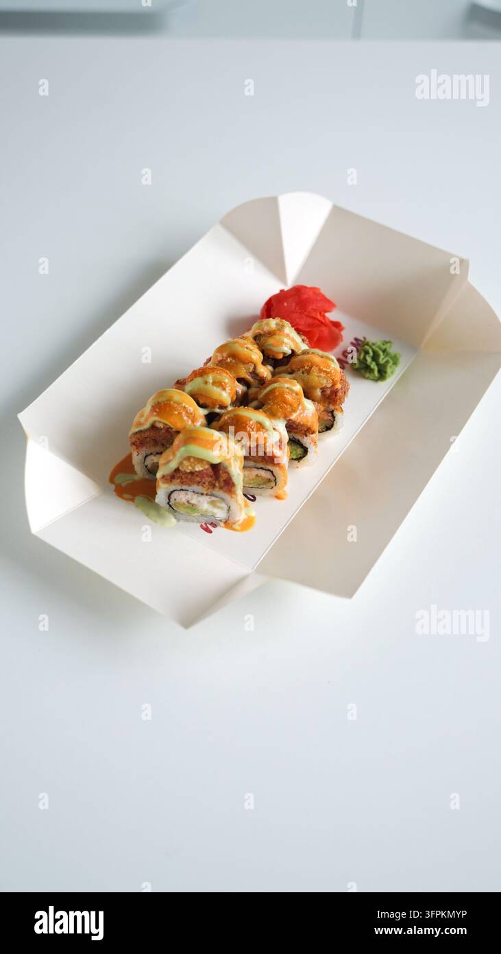 Rotoli di sushi speziati al forno con zenzero e wasabi in contenitore da asporto, un popolare piatto fusion giapponese Foto Stock