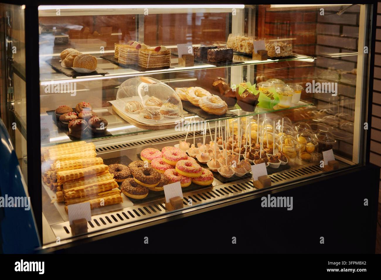 Pasticcini e dolci assortiti disposti dietro una vetrina di vetro in una panetteria o in un caffè. La vetrina illuminata mette in risalto dessert dall'aspetto fresco Foto Stock