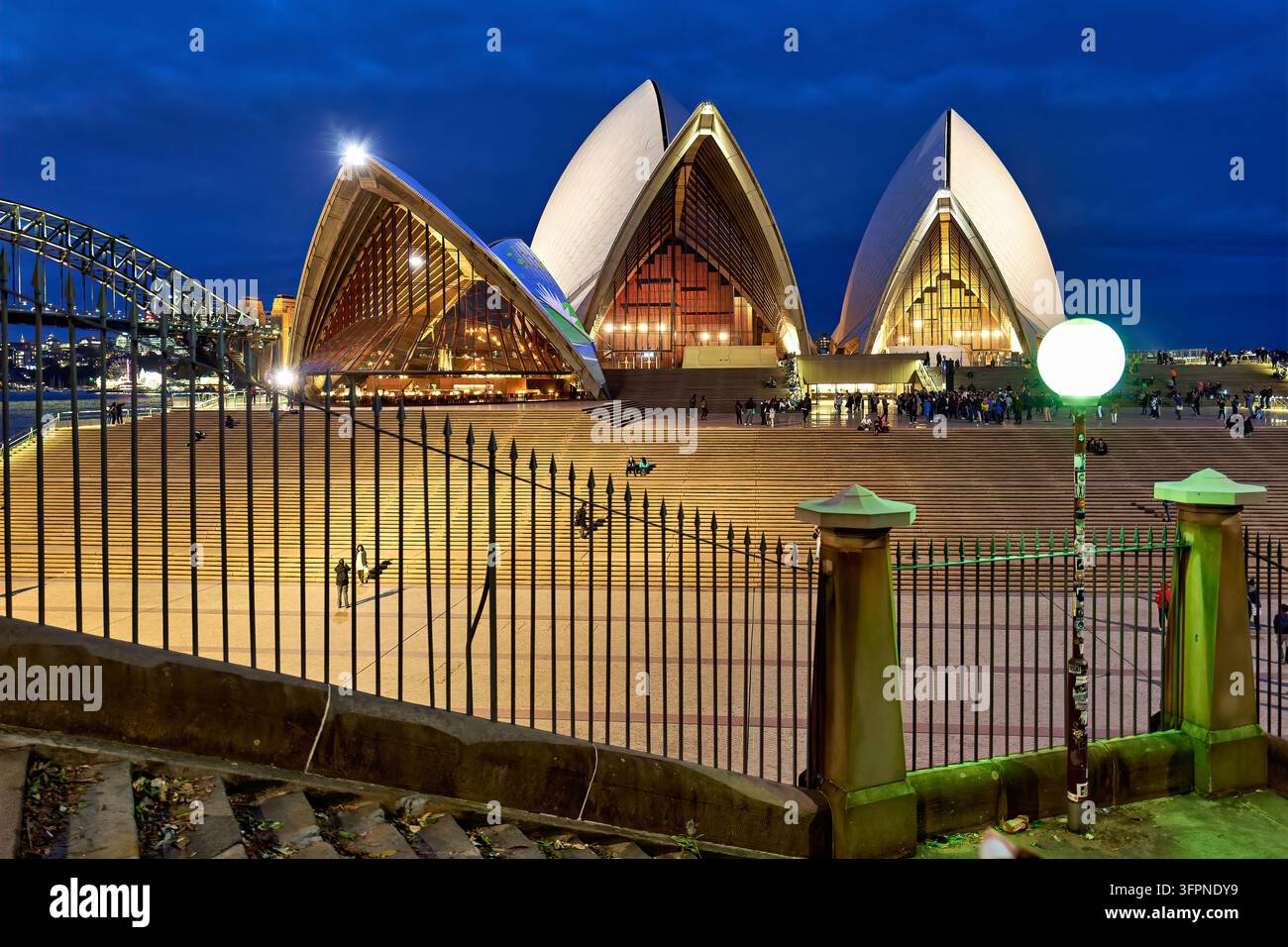 Vele illuminate e gradini del cortile dell'opera su Bennelong Point, Sydney, Australia, visti dietro ringhiere di ferro in una sera d'inverno. Foto Stock
