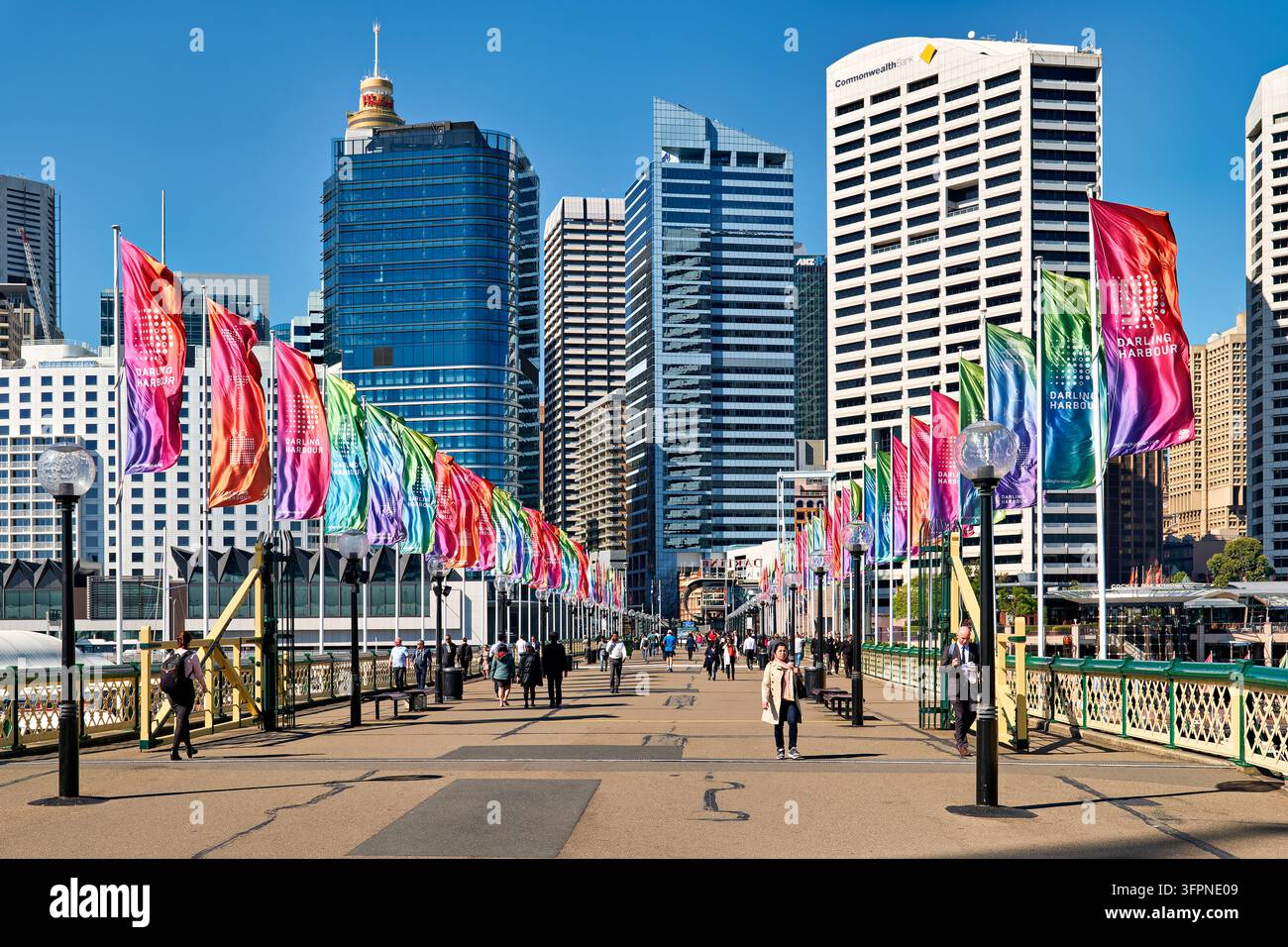I pedoni passano davanti a striscioni colorati verso lo skyline del CBD di Sydney e la Sydney Tower in una giornata invernale soleggiata nel New South Wales, Australia. Foto Stock