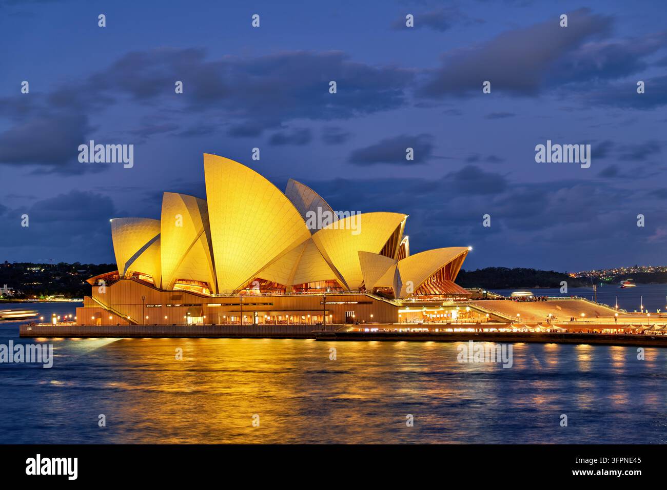 I gusci del tetto a forma di vela illuminati da fari del landmark di Jorn Utzon su Bennelong Point brillano sulla Sydney Harbour, New South Wales, al crepuscolo. Foto Stock