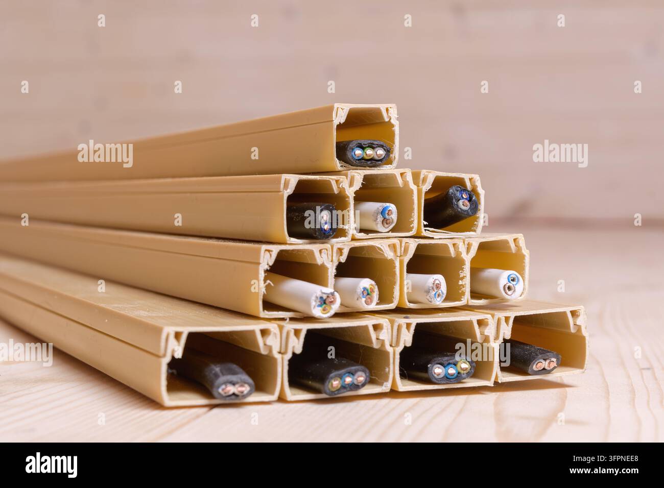 Canali per cavi in plastica pieni di vari cavi elettrici formano una piramide su un pavimento di legno, evidenziando soluzioni di gestione dei cavi sicure e ordinate per Foto Stock