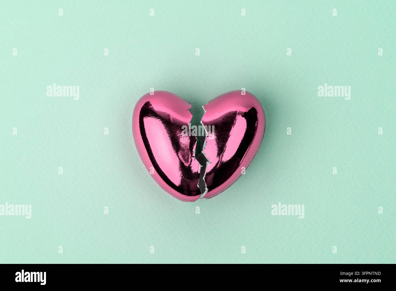 Cuore rosa frantumato su sfondo menta, che simboleggia il dolore al cuore, l’amore perduto e il dolore emotivo. Foto Stock
