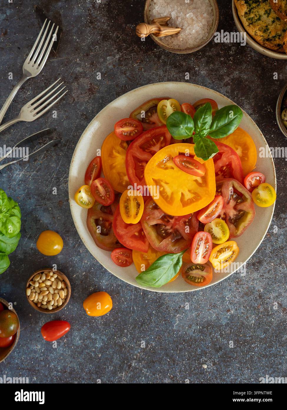 Pomodori colorati con basilico fresco disposti su un piatto bianco in una composizione dall'alto Foto Stock