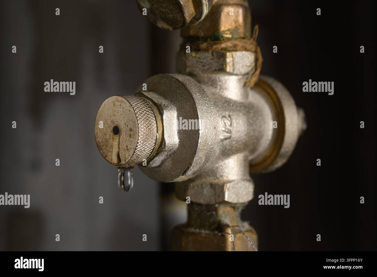 Regolatore della pressione dell'acqua che perde su un tubo metallico in una stanza di servizio buia segnala un guasto idraulico domestico e la necessità di un servizio urgente. Foto Stock