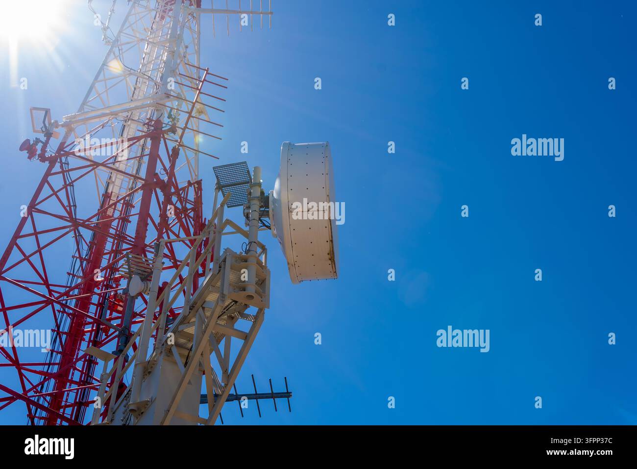 Una torre di comunicazione rossa e bianca con antenne e parabole si erge contro un cielo blu limpido. Foto Stock