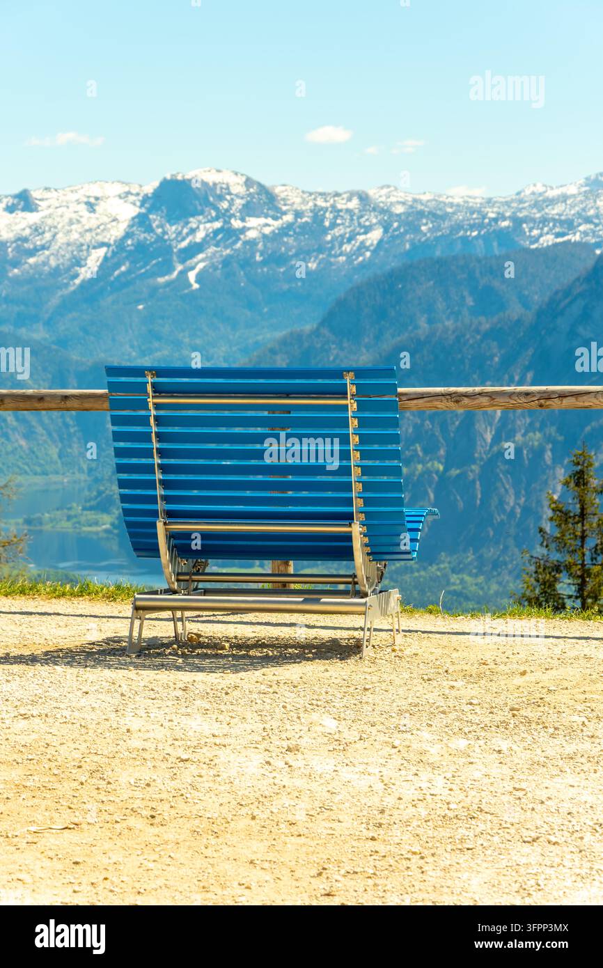 Una panchina blu si affaccia su una catena montuosa innevata sotto un cielo sereno. Foto Stock