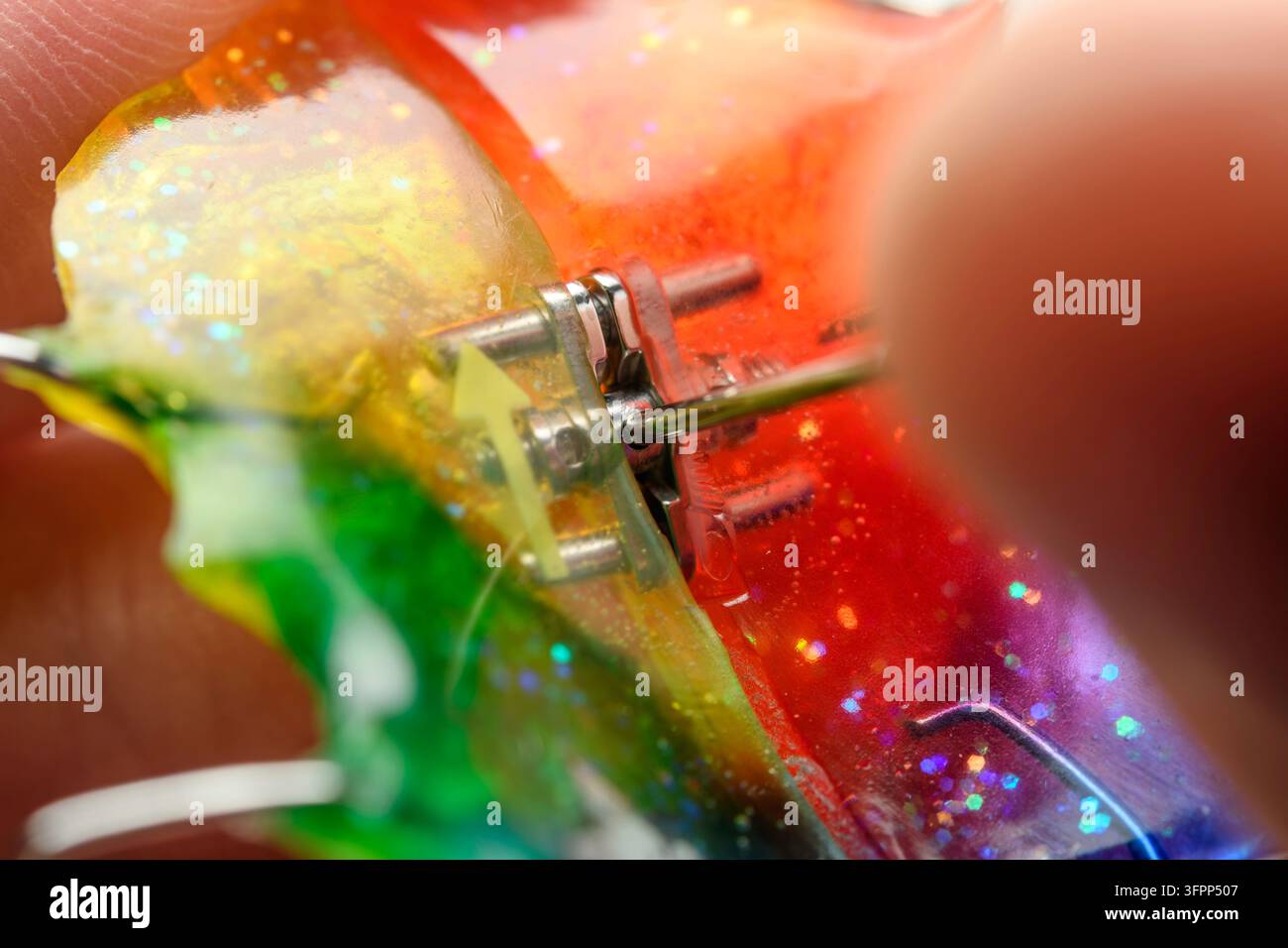 Mano vicina stringe una vite metallica del mantenitore espansore palatino arcobaleno luccicante, dettaglio macro con sfondo clinico sfocato morbido. Foto Stock
