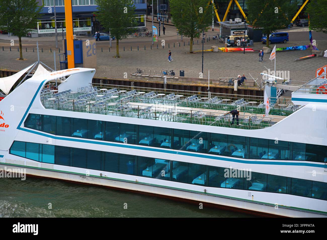Rotterdam, Paesi Bassi – 07.19.2026 Una nave da crociera fluviale con un ponte superiore aperto, tavoli e una persona in uniforme che pulisce o si occupa del ponte Foto Stock