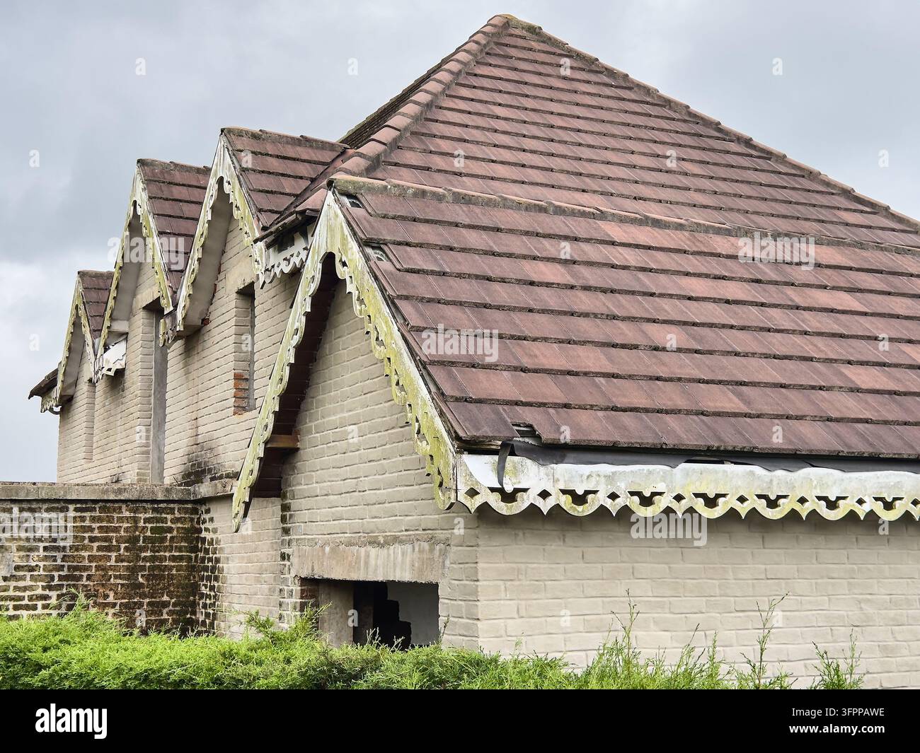 vecchia casa in mattoni abbandonata con tetto di tegole marroni, pannelli decorativi in legno bianco stagionato, vista architettonica esterna, immobiliare vintage Foto Stock