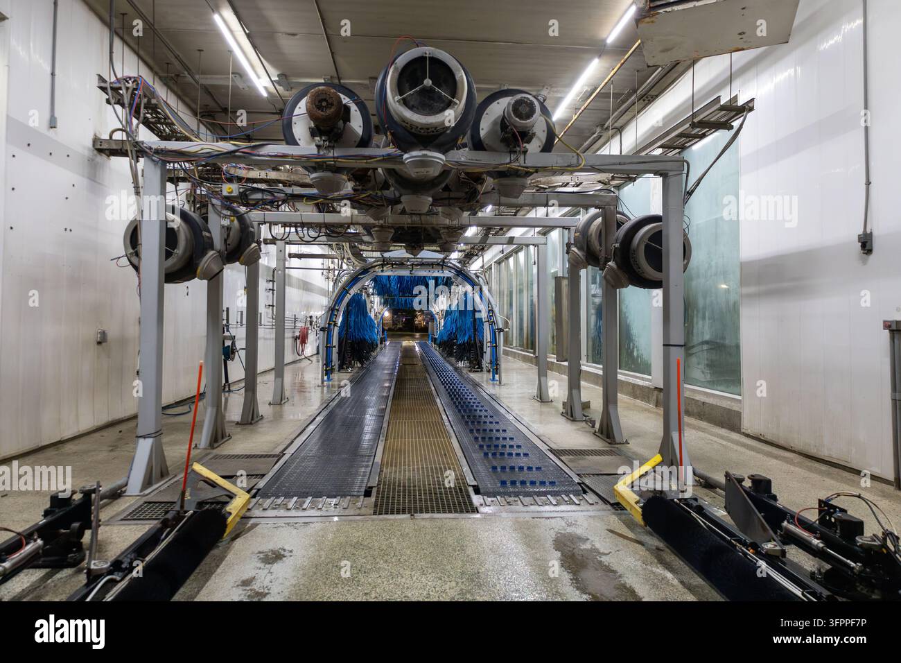 Tunnel di lavaggio automatico vuoto con tracce sul pavimento bagnate, spazzole blu e finestre laterali sporche prima della pulizia dopo l'orario di chiusura. Foto Stock