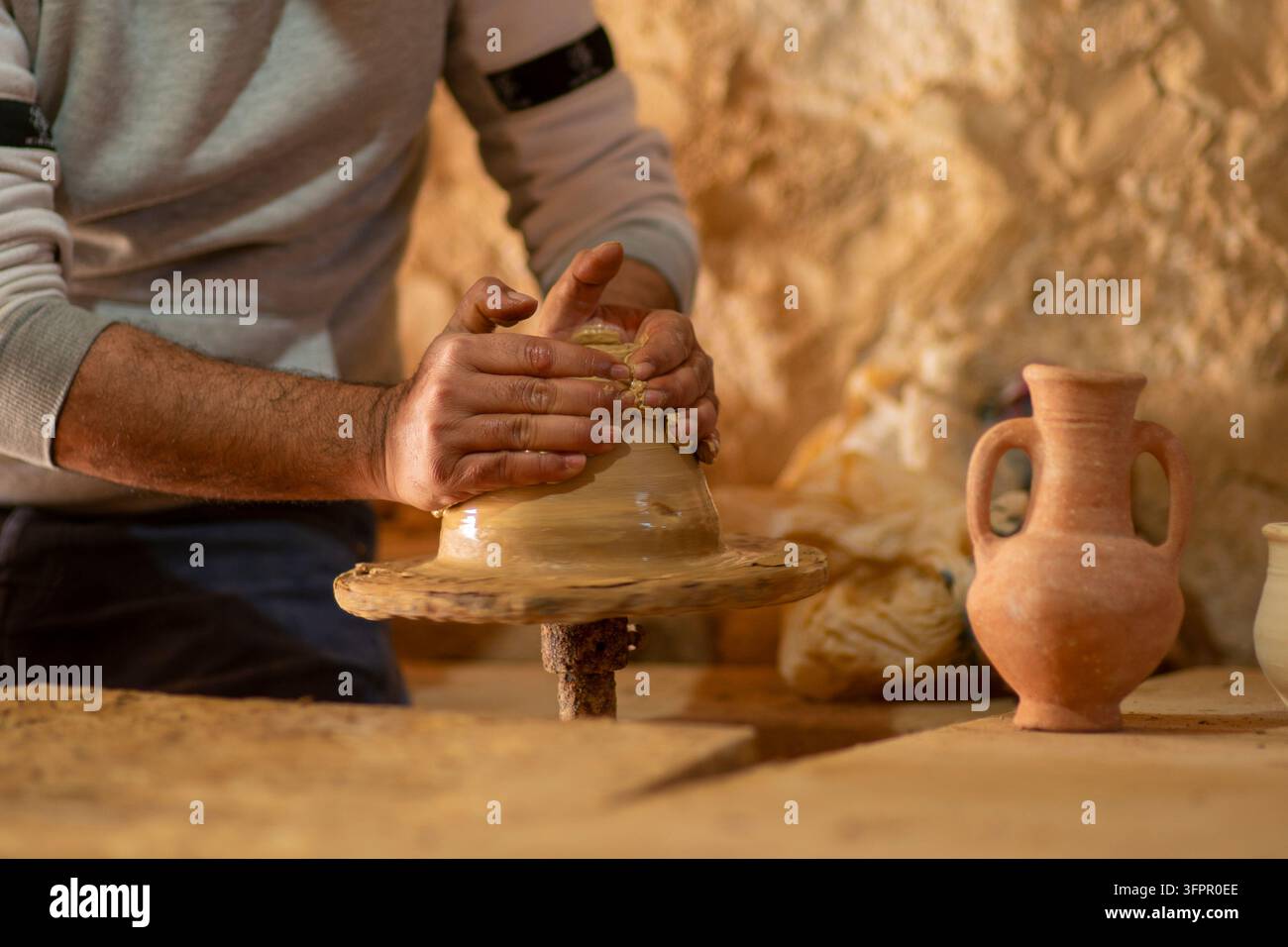 Artigiano esperto che modella argilla bagnata su una ruota da vasaio rotante in un ambiente di bottega tradizionale Foto Stock