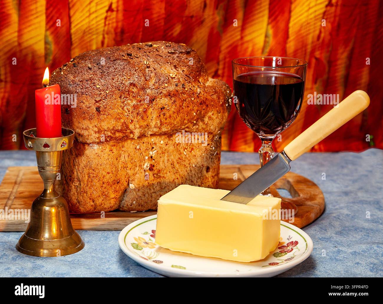 Pane rustico e burro con un bicchiere di vino rosso accanto a una candela accesa che crea un'immagine di natura morta calda e accogliente Foto Stock