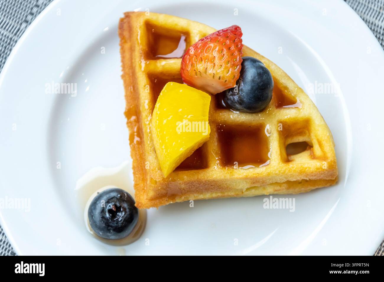Una fetta di waffle dorata guarnita con frutti di bosco freschi e pesca su un piatto di ceramica bianca Foto Stock