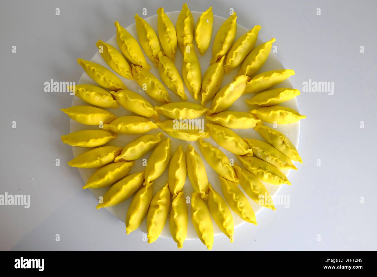 Gnocchi di zafferano gialli vivaci disposti in un motivo circolare di girasole su un piatto bianco. Foto Stock