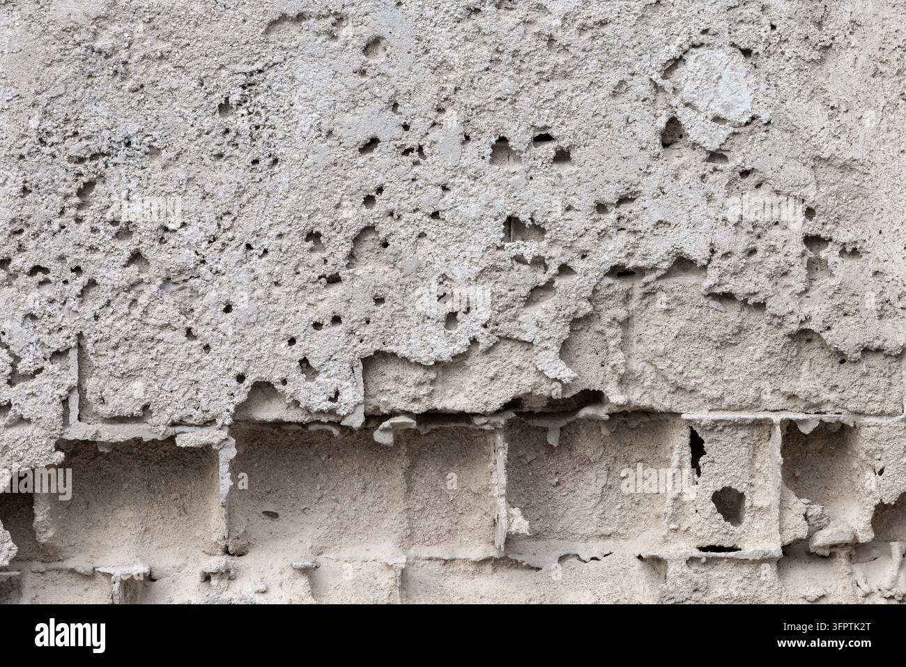 Intonaco di cemento grigio eroso che si stacca da un muro di blocchi di cemento, superficie porosa incavata con blocchi di cenerino esposti e giunti di malta Foto Stock
