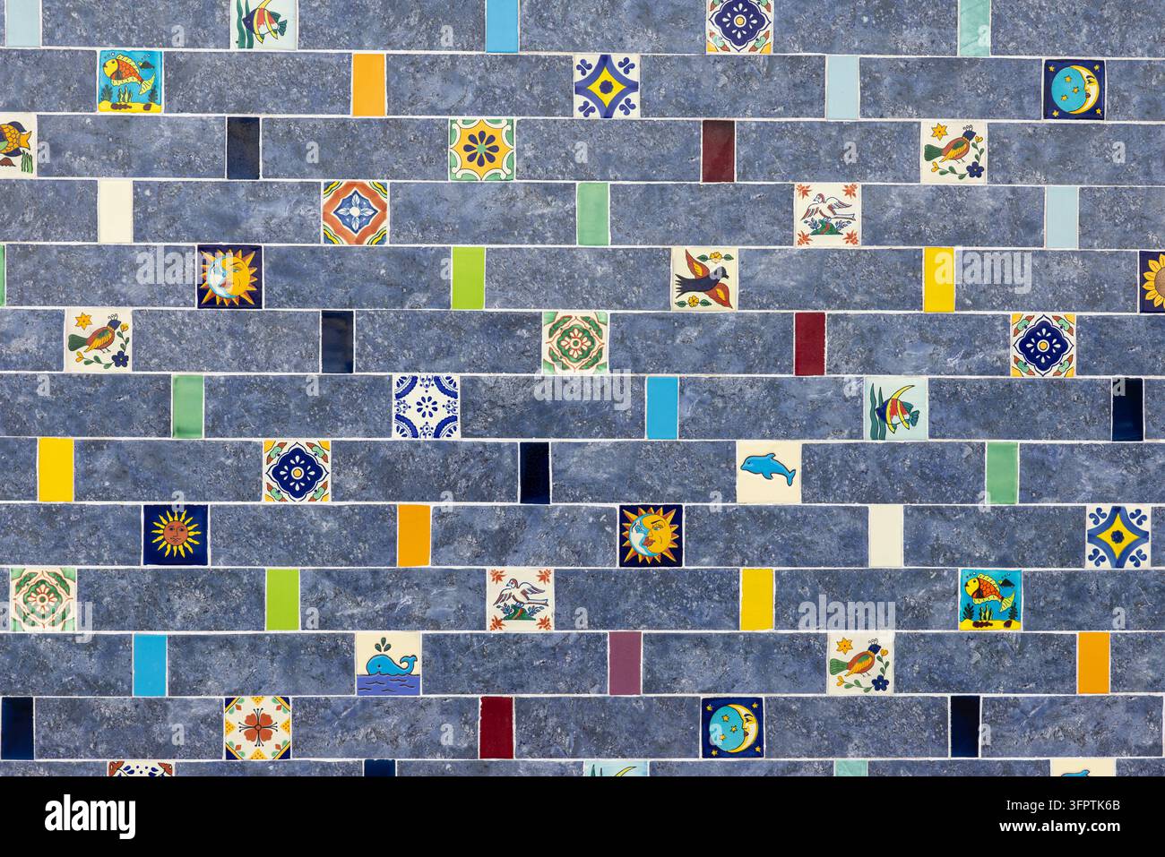 Muro di piastrelle in pietra grigio blu con piastrelle decorative colorate dipinte a mano sparse a forma di sole, luna, uccello, pesce e balena, disposizione a mattonelle stile metropolitana Foto Stock