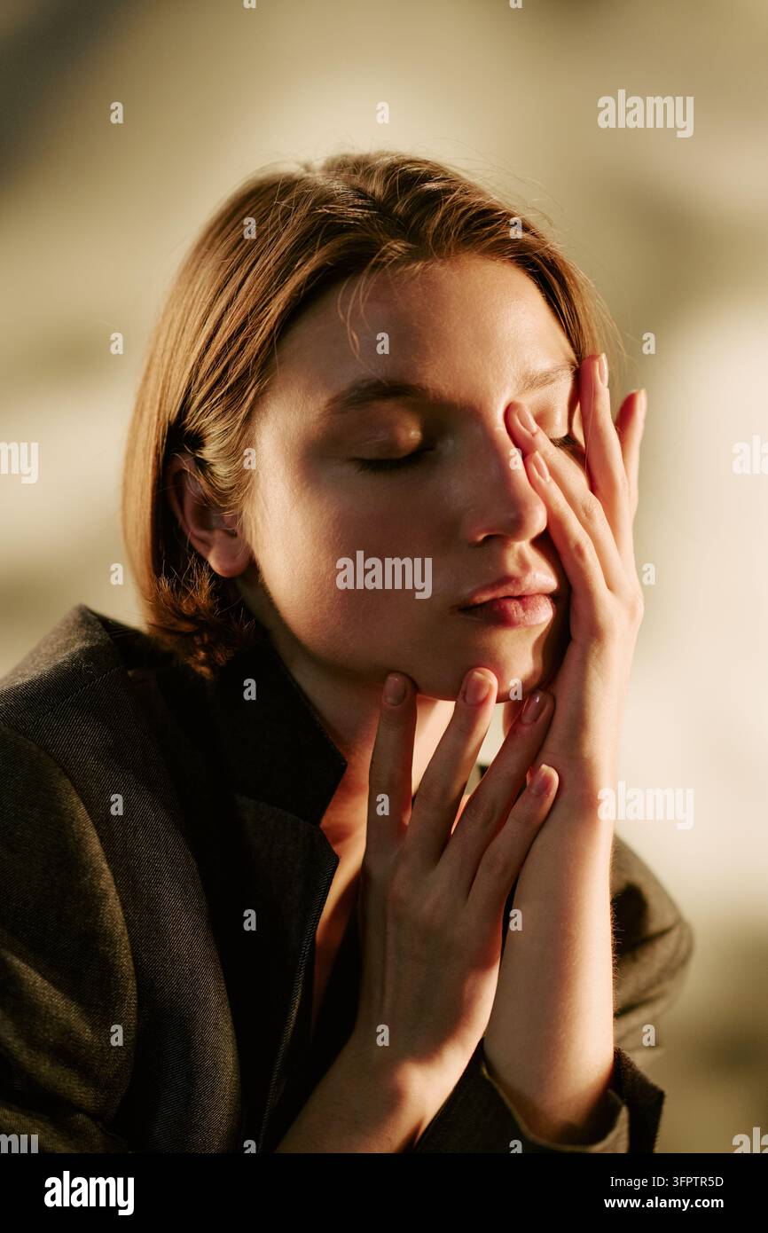 Donna che tocca il viso con gli occhi chiusi in studio per il benessere mentale Foto Stock