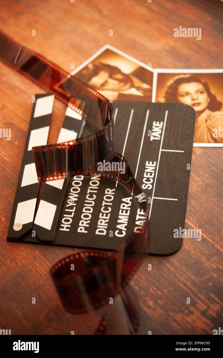 natura morta cinematografica seppia con una claquette di film hollywoodiana, una striscia di film arricciata e due fotografie di ritratto in stile vintage su legno Foto Stock
