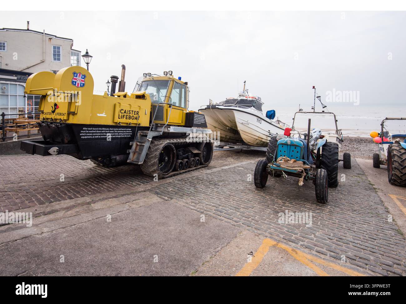Trattore cingolato Caterpillar Challenger modificato dai Cantieri Habbeke per lanciare imbarcazioni di salvataggio e battelli di salvataggio dalle spiagge, accanto a un trattore vintage blu. Foto Stock