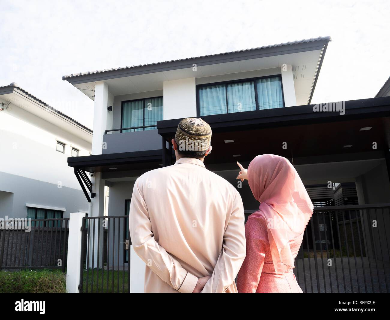 Proprietari di casa. Vista posteriore di una coppia musulmana amorevole che indica e guarda la loro casa dei sogni. Celebrazione dell'acquisto di un nuovo immobile Foto Stock