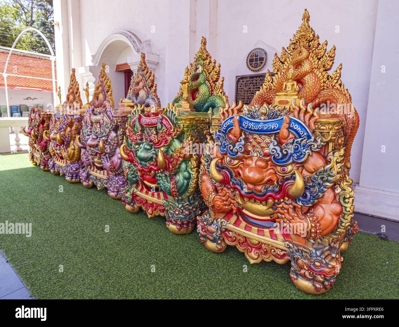 Muang, Phayao, Thailandia - 02 ottobre 2026: Wat Sri Khom Kham, fila di cassette per le donazioni a forma di leone in arancione, verde e oro con striscioni di testo thailandesi Foto Stock