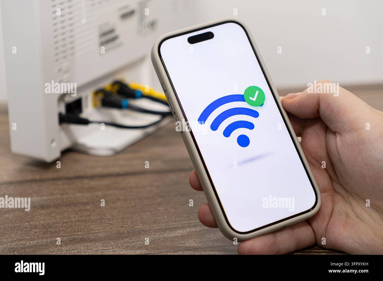 Una persona tiene un dispositivo mobile che mostra un'icona di segnale Wi-Fi confermata accanto a un modem a banda larga per illustrare la configurazione stabile del servizio Internet e moderna t Foto Stock
