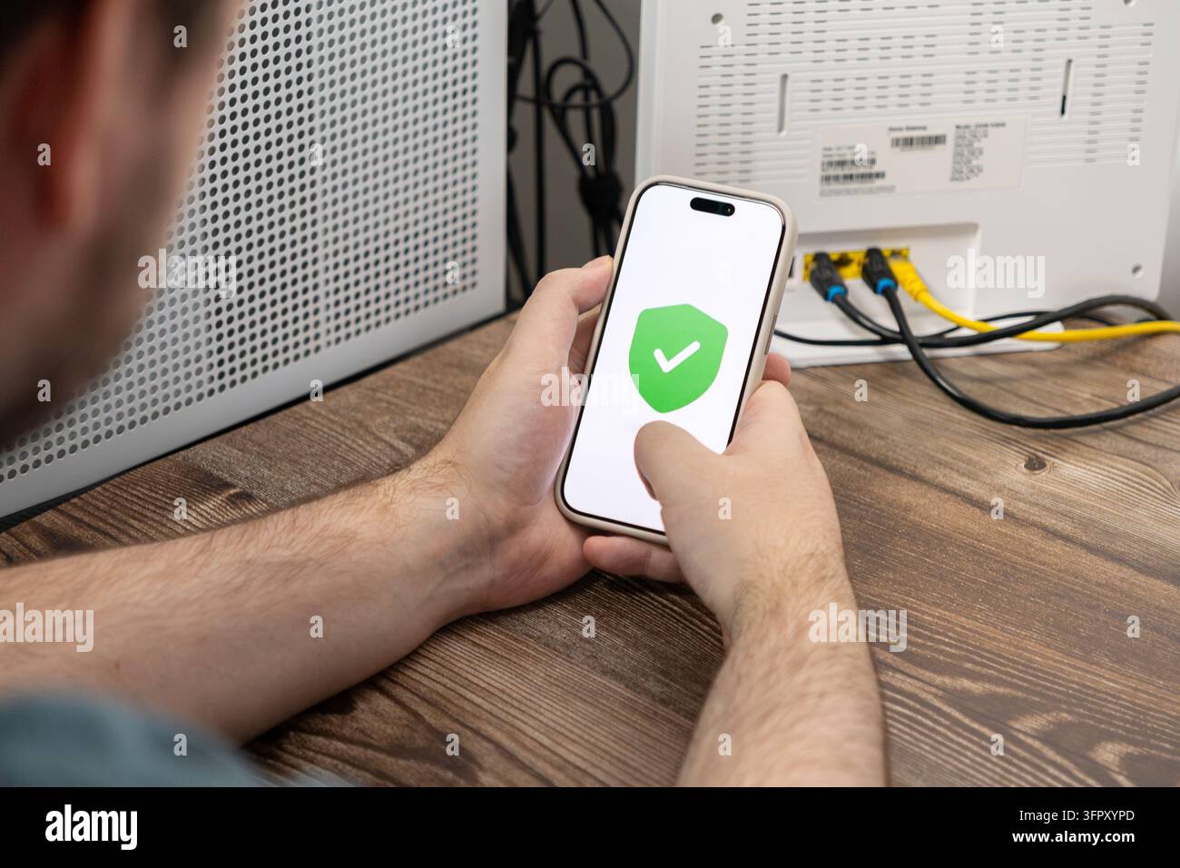Una persona controlla un dispositivo mobile che mostra un simbolo di sicurezza verde per confermare la connettività Internet crittografata, rappresentando la consapevolezza della cybersecurity coni Foto Stock