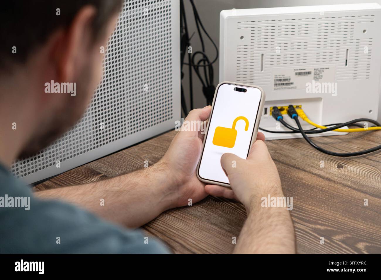 L'utente controlla le impostazioni di sicurezza su un dispositivo mobile mentre è seduto accanto a un router di rete, illustrando la manutenzione tecnica, la protezione digitale e la connessione Foto Stock