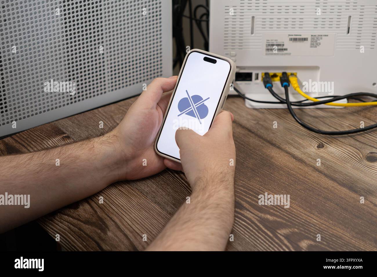 Prima piano di mani che utilizzano un dispositivo mobile con un'icona di nuvola offline mentre sono posizionate accanto a un gateway a banda larga cablato, illustrando un guasto tecnologico Foto Stock