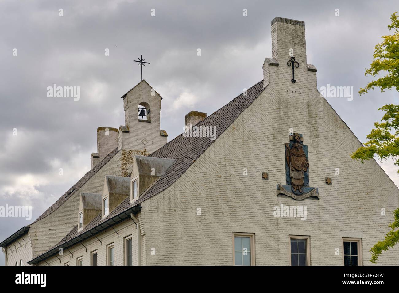 Moerdijk, Paesi Bassi – 4 giugno 2026: Edificio conventuale tradizionale in mattoni bianchi del 1948 con timpani a gradini e scultura religiosa, architettura storica in un villaggio di fronte all’espansione della zona industriale. Foto Stock