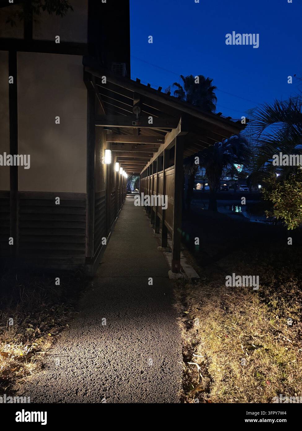 Un lungo corridoio esterno coperto dell'edificio del resort termale delle sorgenti calde di Amandi di notte, illuminato da calde lanterne a muro sotto un cielo crepuscolare blu scuro. Foto Stock