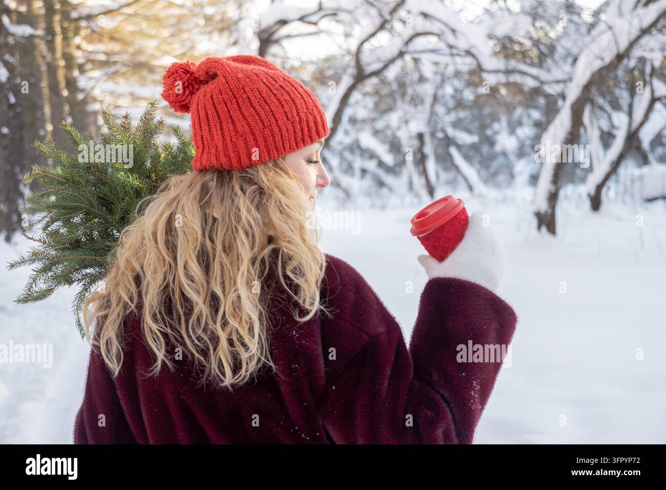 Donna che tiene un caffè da asporto e rami di abete in una foresta invernale Foto Stock