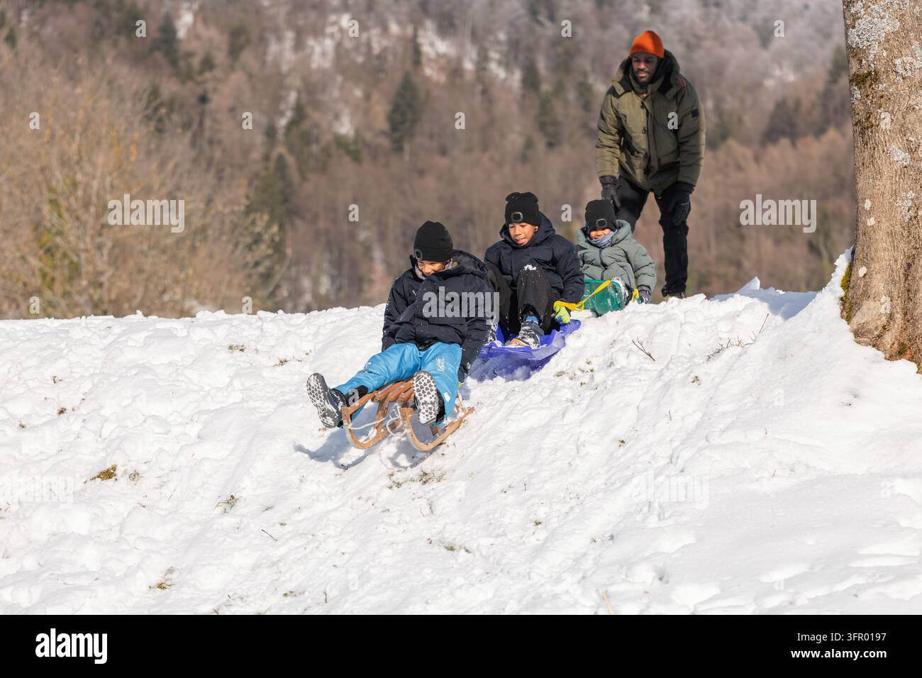Padre e figli gioiosi trascorrono del tempo di qualità facendo slittino all'aperto, godendo della convivialità familiare e del divertimento invernale spensierato nella neve. Foto Stock